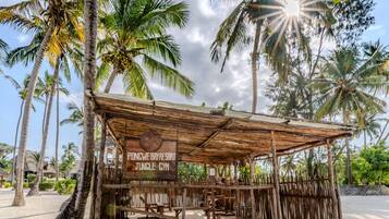 Eine Holzkonstruktion mit der Aufschrift 'Pongwe Bay Resort Jungle Gym', umgeben von sandigem Boden und Palmen im Hintergrund.