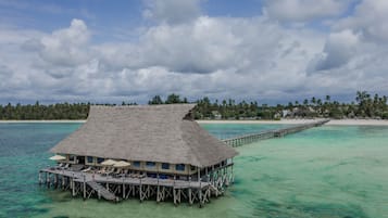 An overwater bungalow with a thatched roof, multiple lounge chairs, and a wooden deck.