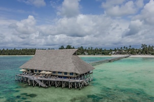 An overwater bungalow with a thatched roof, multiple lounge chairs, and a wooden deck.