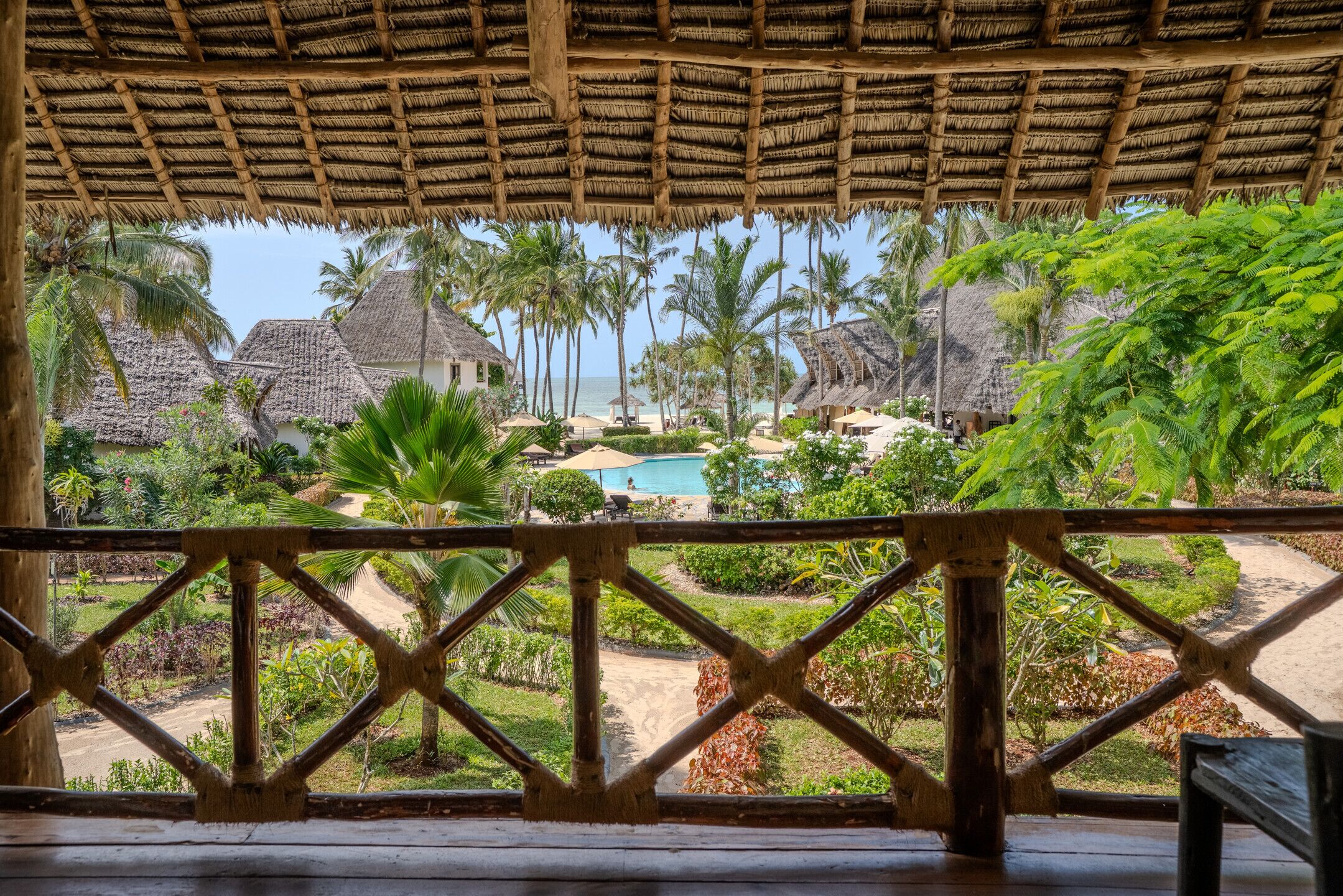 A resort with thatched-roof buildings, a swimming pool, and lush tropical vegetation.