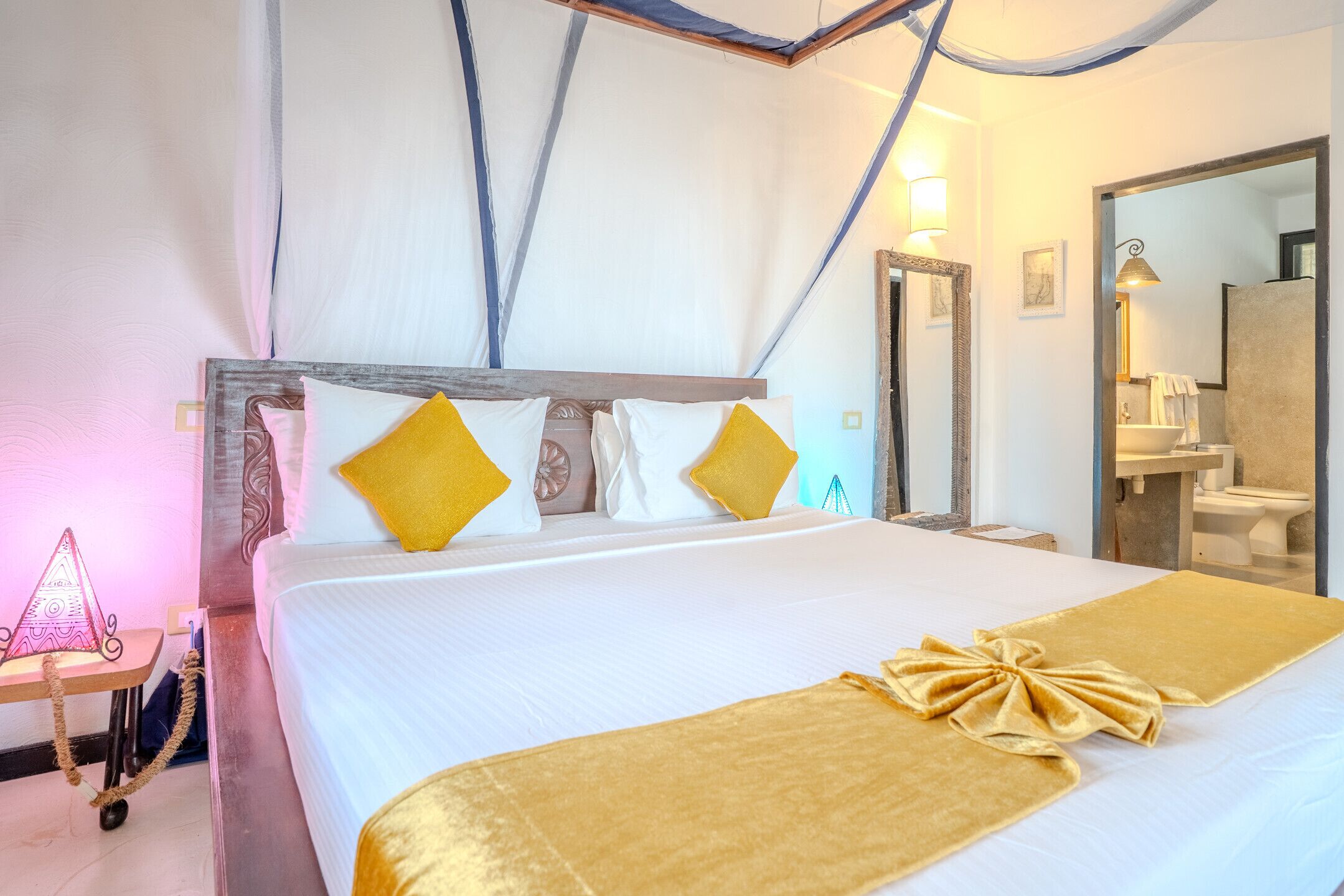 A hotel room with a bed, a bedside table, a mirror, and a bathroom visible through an open door.