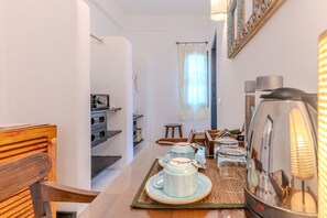 Uma área de refeições com uma mesa posta para dois, uma cafeteira e uma chaleira à direita.