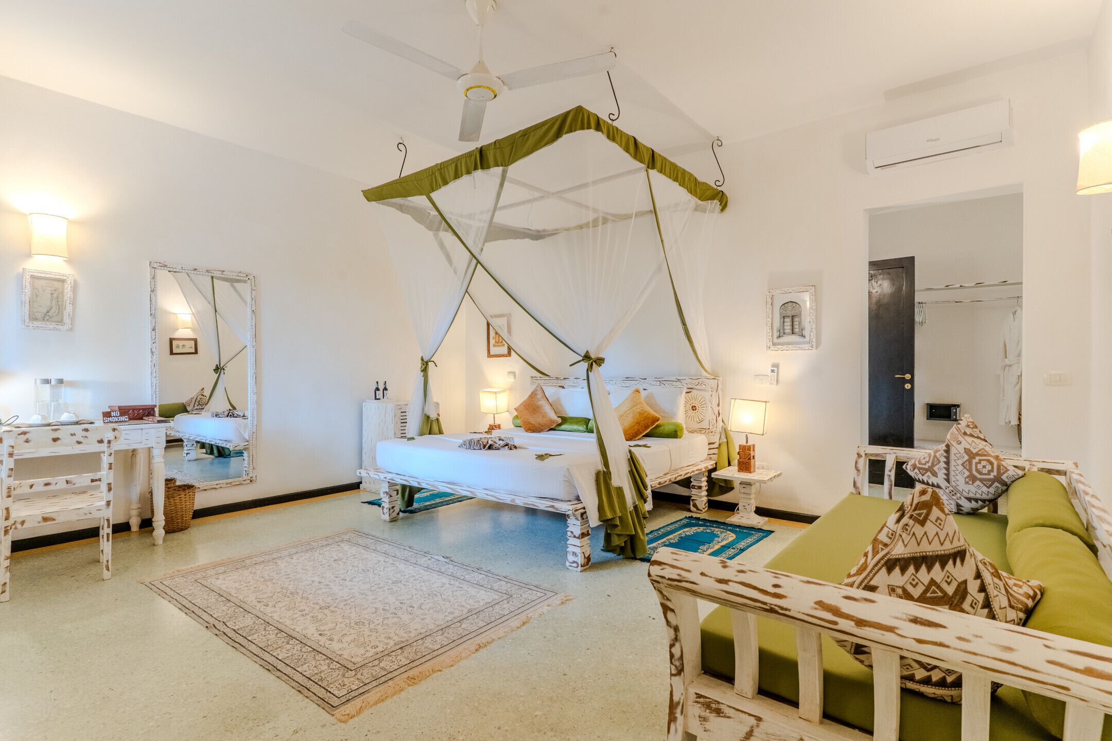 Ein Schlafzimmer mit Himmelsbett, Nachttischen, einem Schminktisch und einem grünen Sofa, sowie einem gemusterten Teppich.