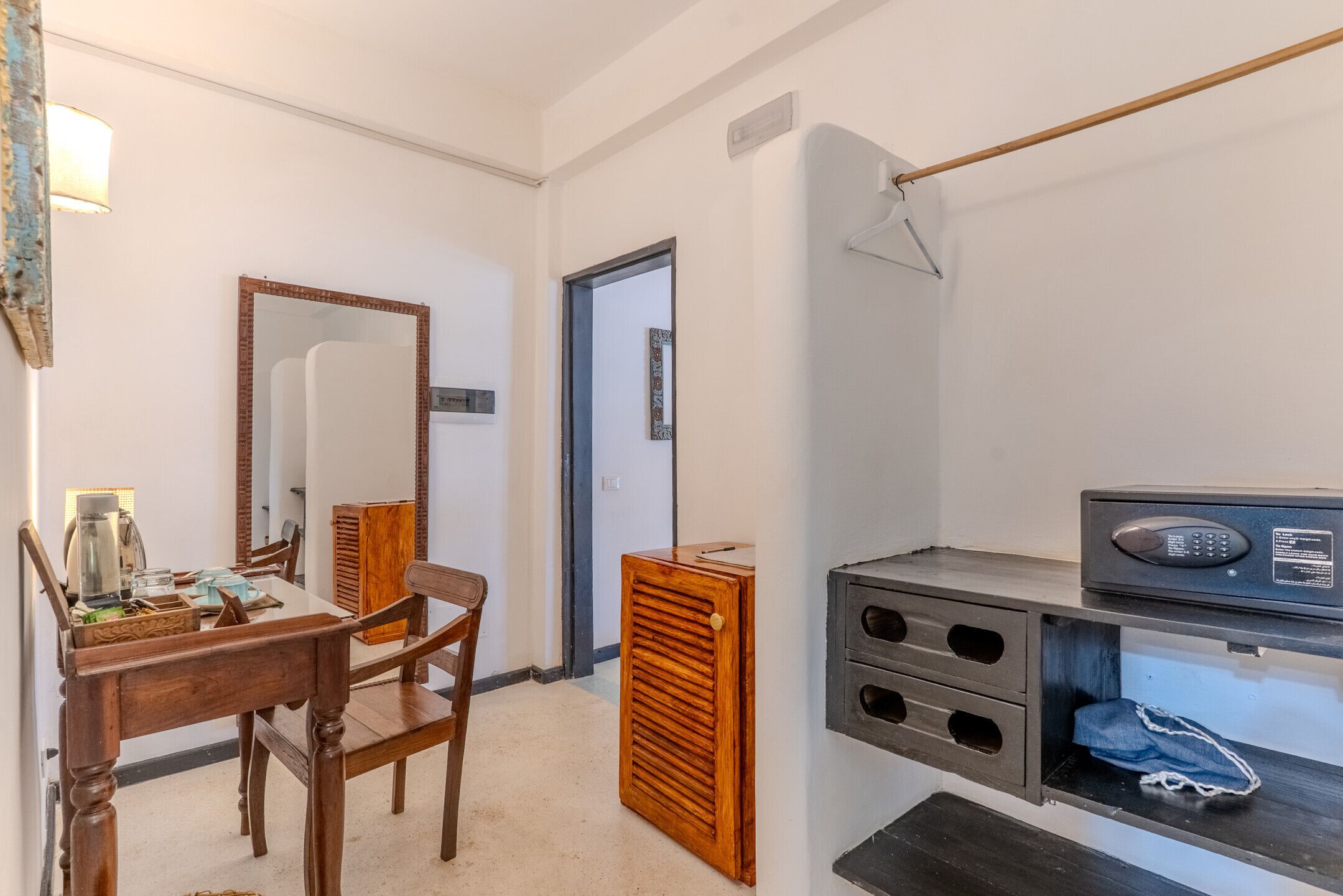 Een kamer met een houten eettafel, stoelen, een spiegel, een kledingkast en een magnetron.