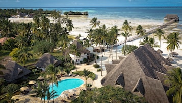 Un resort con piscina, construcciones de techo de paja, palmeras y vista a la playa.