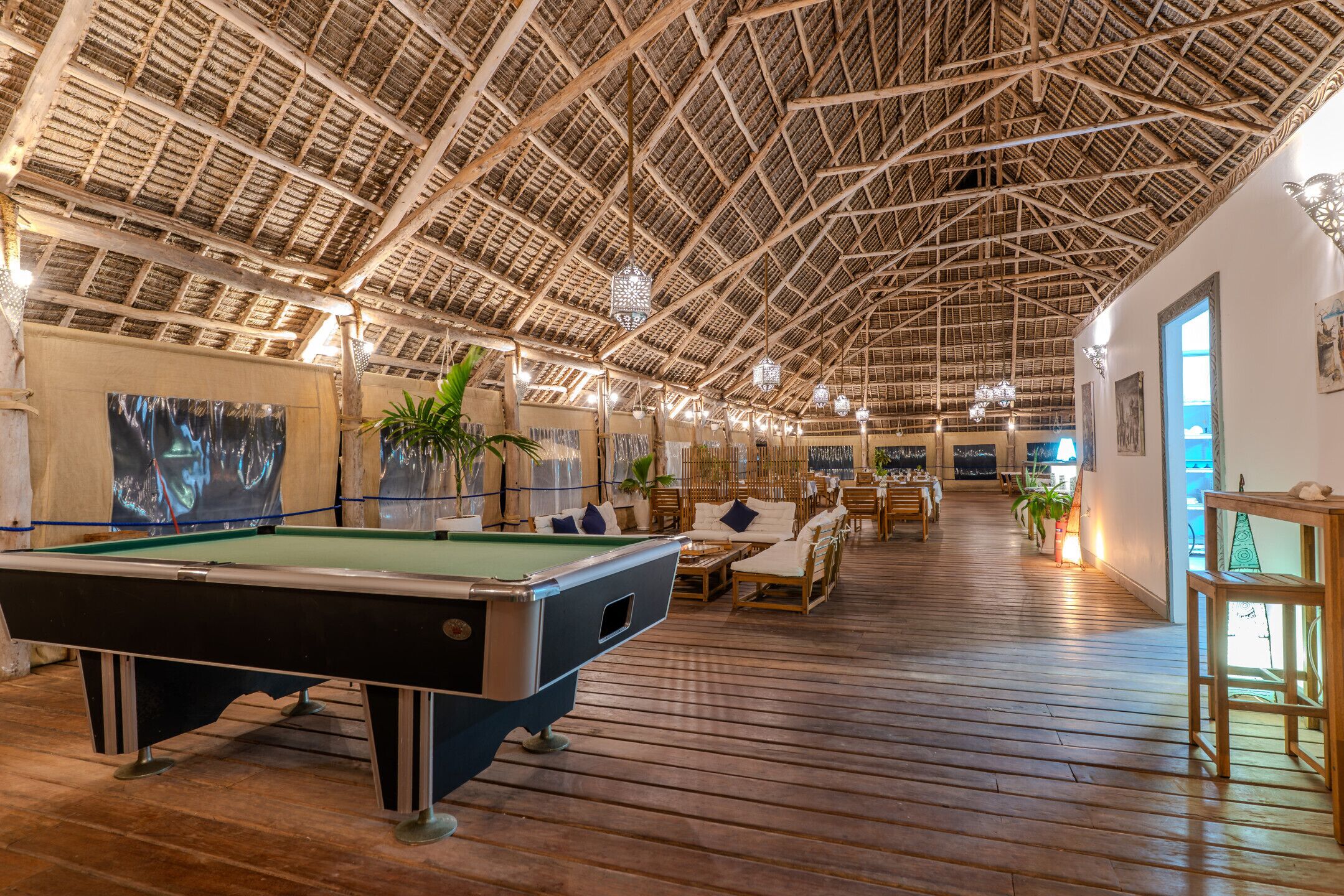 A spacious indoor area with a pool table, wooden flooring, and a high ceiling with a thatched roof design.