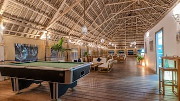 A spacious indoor area with a pool table, wooden flooring, and a high ceiling with a thatched roof design.