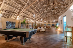 A spacious indoor area with a pool table, wooden flooring, and a high ceiling with a thatched roof design. - Pongwe Bay Resort (Pongwe)