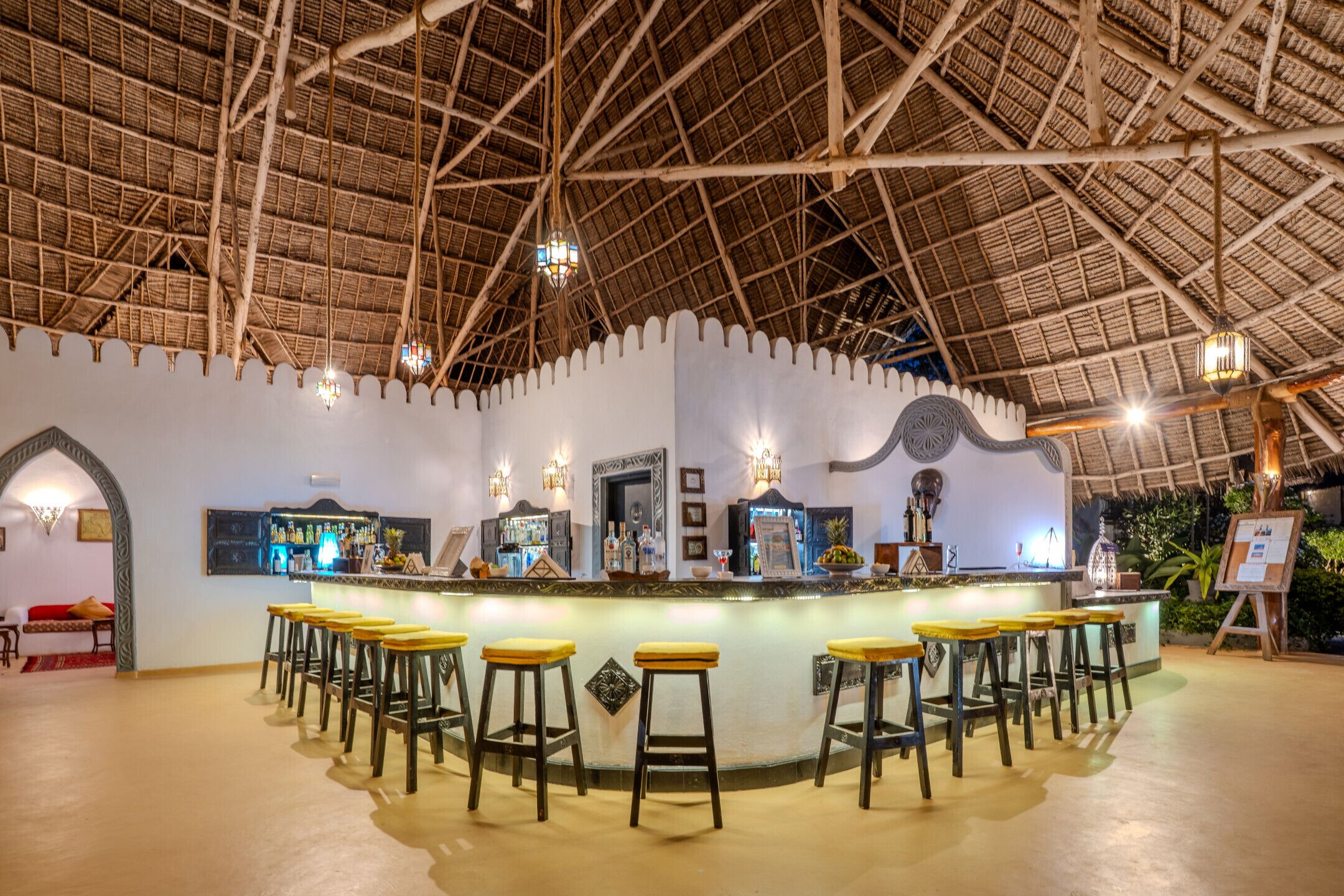 A bar area with stools, a counter, and a thatched roof ceiling.