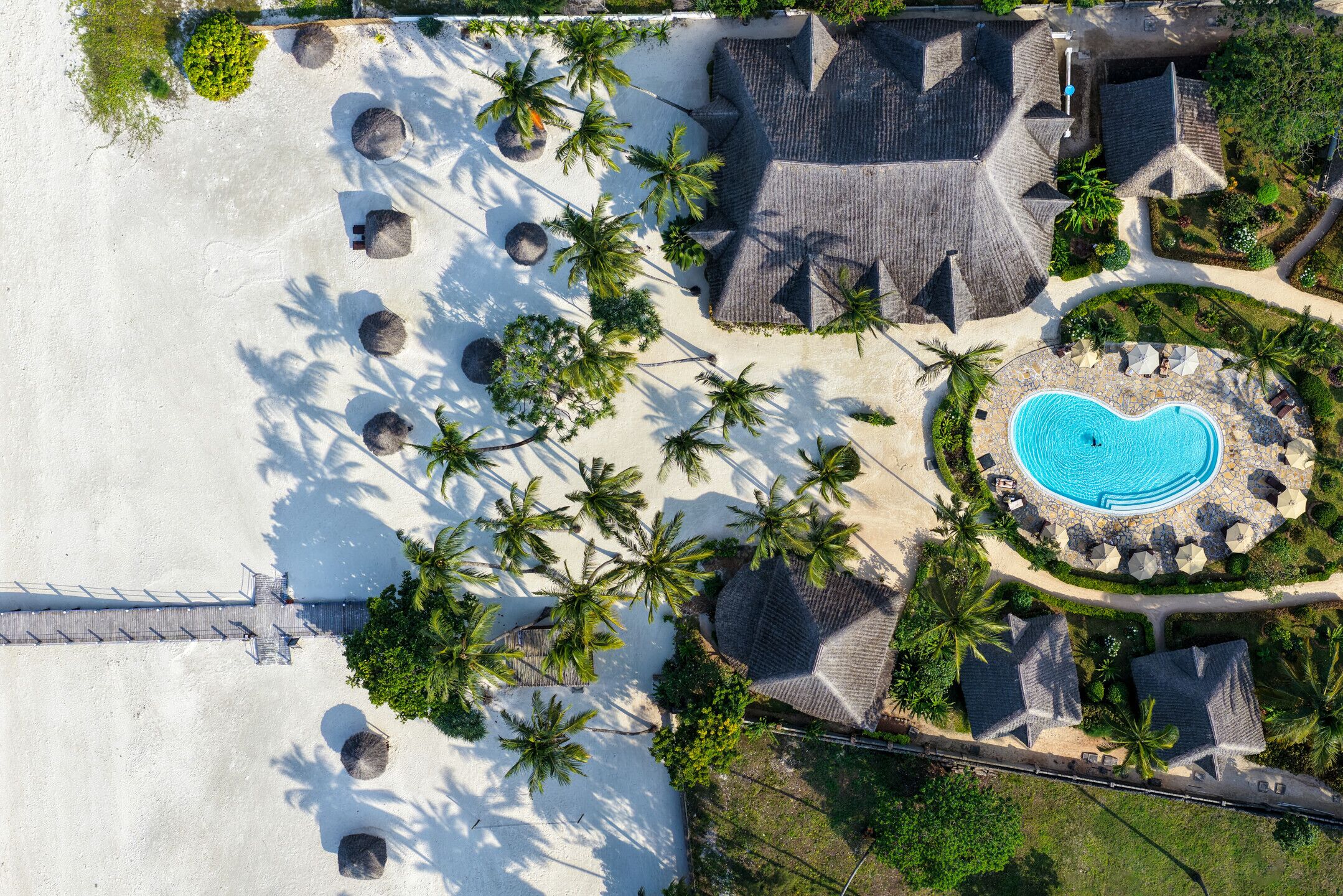 Luftaufnahme eines Resorts mit Schwimmbad, Palmen und Strand.