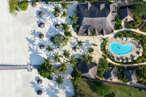 Vue aérienne d’un complexe hôtelier avec une piscine, des palmiers et une plage.