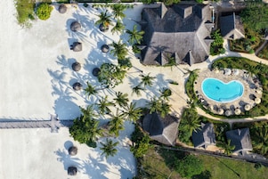Vista aérea de un complejo turístico con piscina, palmeras y zona de playa.