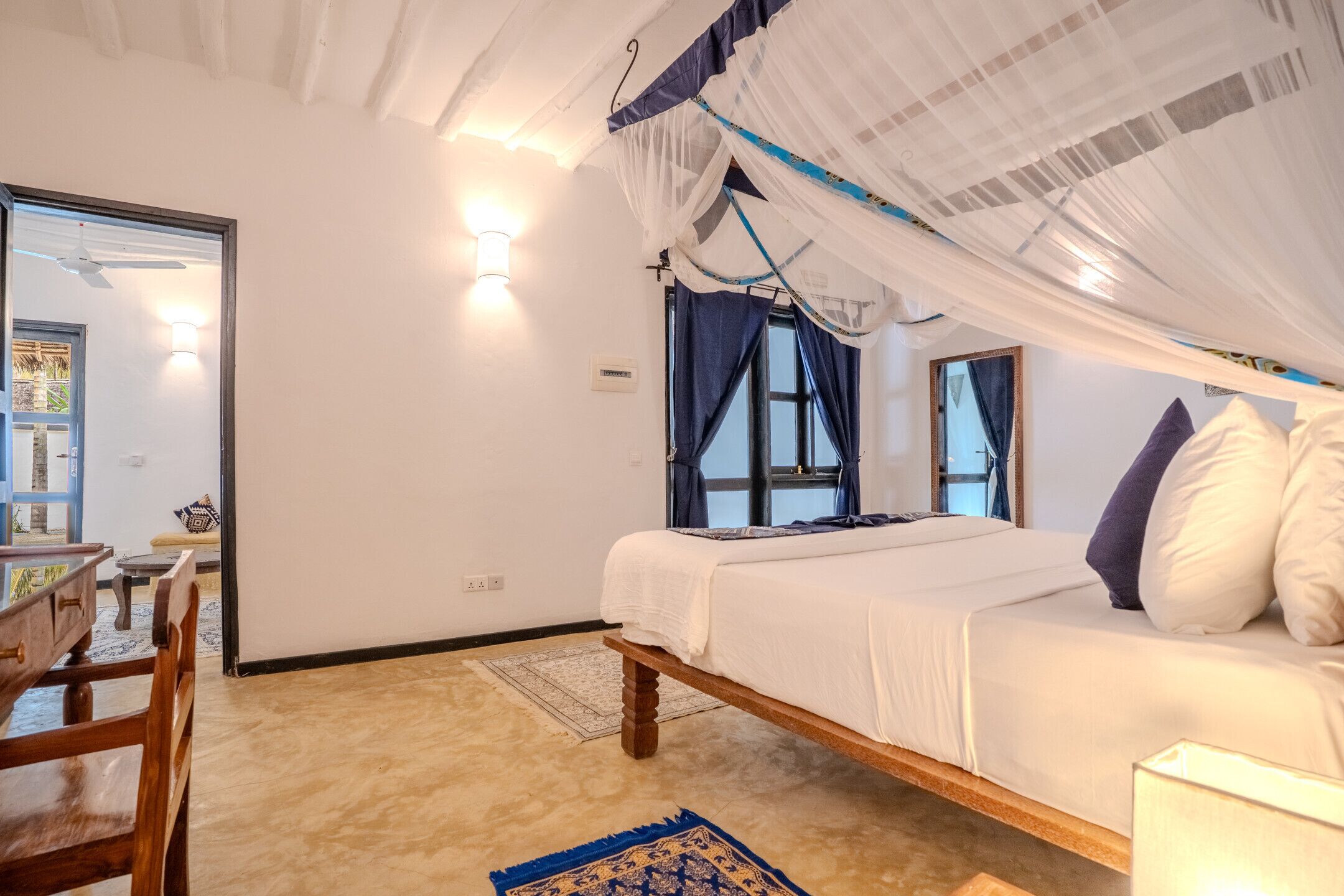 A bedroom with a bed, a chair, a desk, and a window with curtains.
