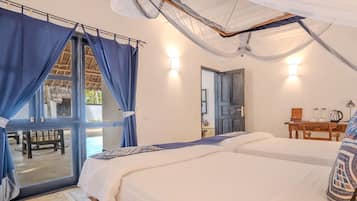 Une chambre avec deux lits, une fenêtre avec des rideaux, une porte et une petite table avec une lampe.
