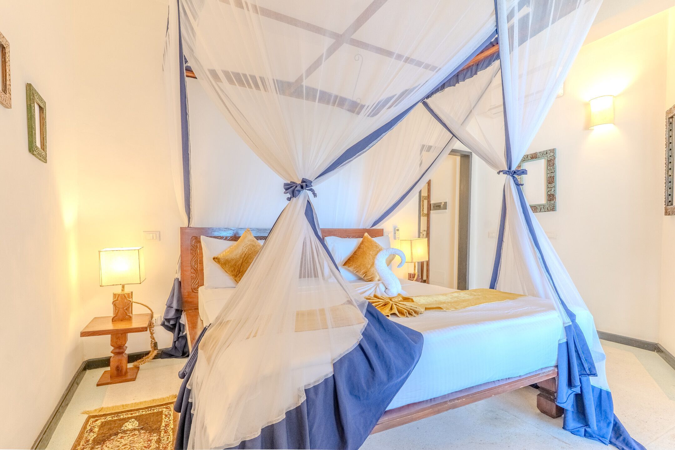 A bedroom with a four-poster bed, a nightstand, a lamp, and a mirror.