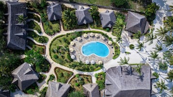 Un resort con piscina central, rodeado de jardines ajardinados y varias construcciones tipo bungalow.