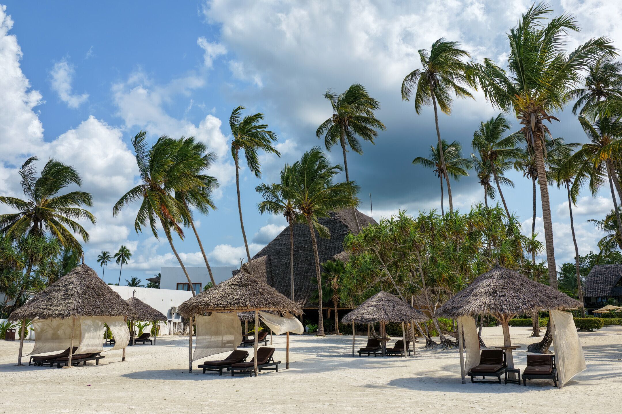 A beach resort with thatched-roof huts, palm trees, and sun loungers.
