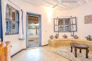 A room with a sofa, a round table, a ceiling fan, a window with a view, and a door leading outside. - Pongwe Bay Resort (Pongwe)