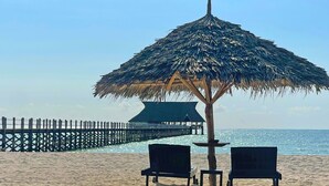 A beach with a thatched umbrella, two chairs, and a pier in the background. - Pongwe Bay Resort (Pongwe)