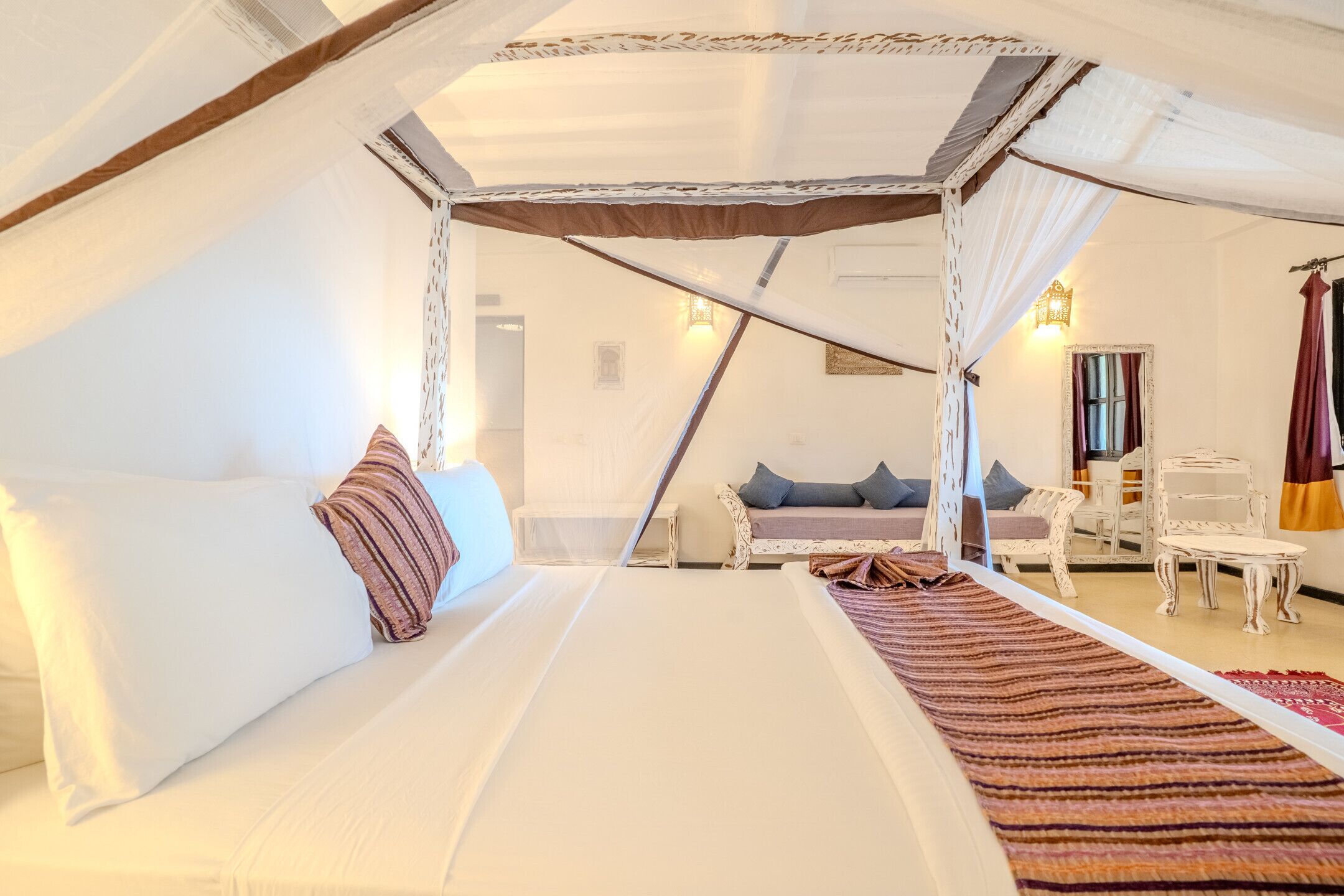 A bedroom with a canopy bed, a sofa, a small table, and a mirror.