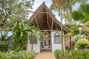 A traditional thatched-roof structure with a central doorway, surrounded by lush tropical vegetation. - Pongwe Bay Resort (Pongwe)