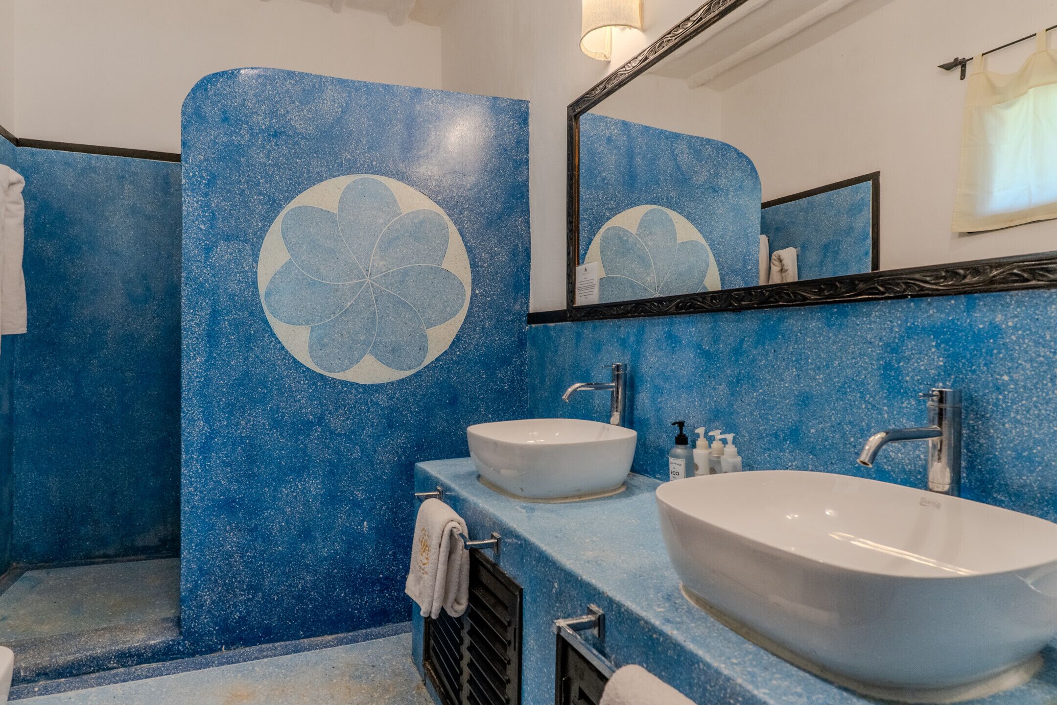 Un baño con pared azul moteada, un espejo grande, dos lavamanos y un perchero para toallas.