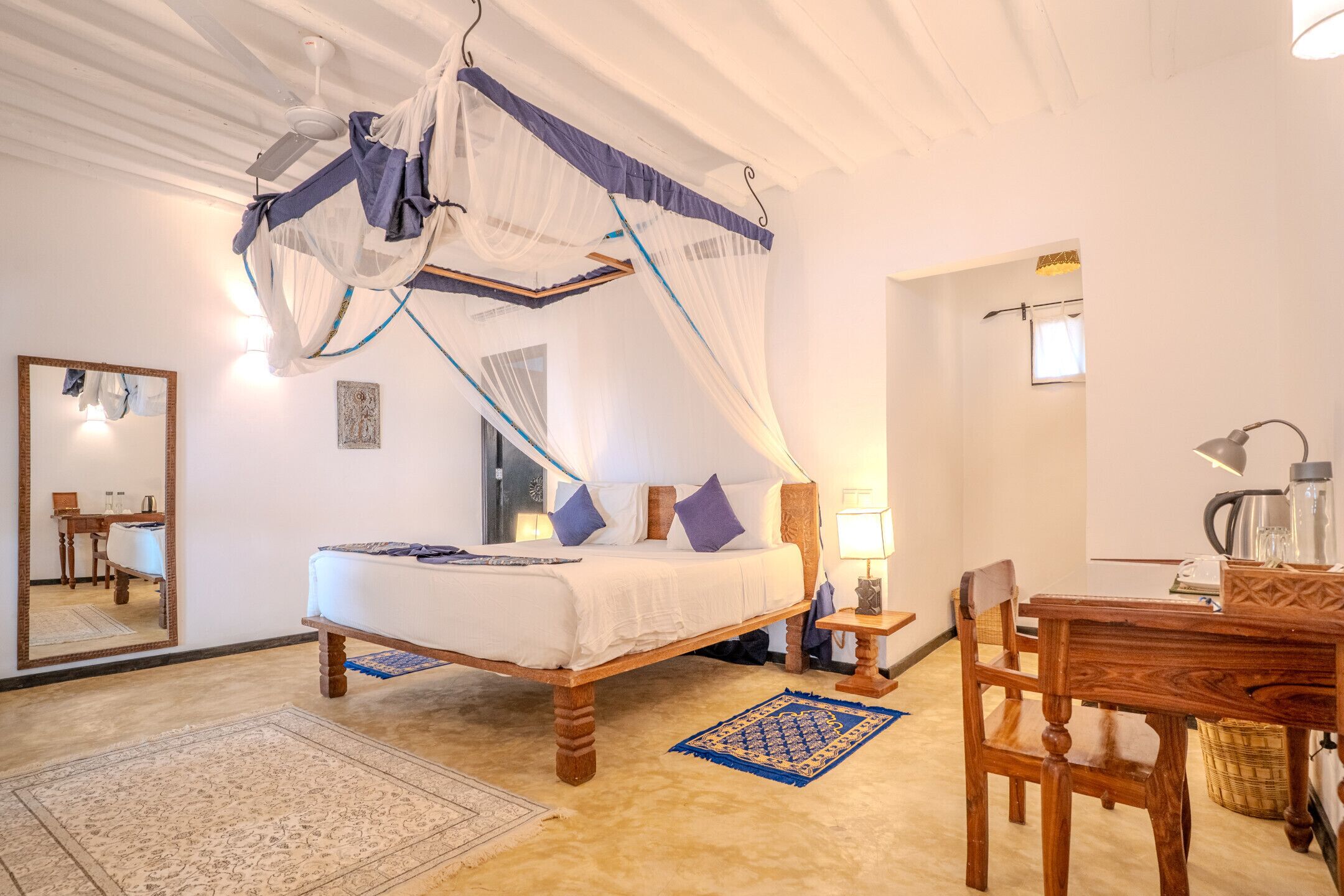 Quarto com cama de dossel, escrivaninha, cadeira, abajur e espelho.