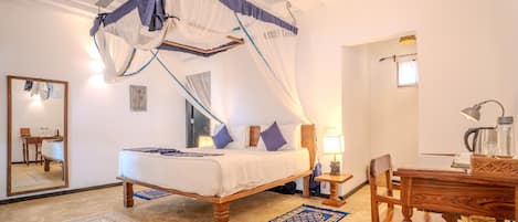 Quarto com cama de dossel, escrivaninha, cadeira, abajur e espelho.