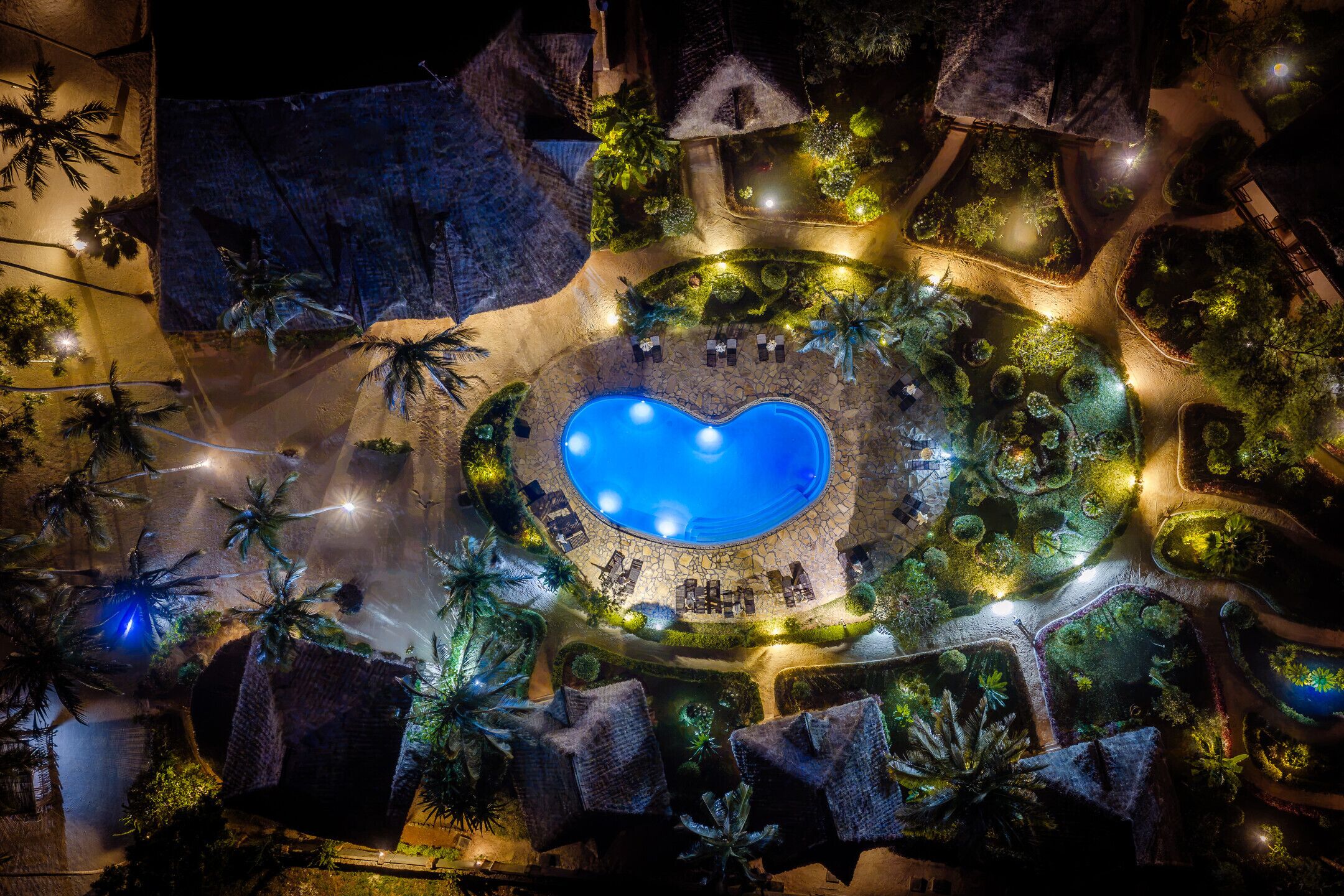 Vista aérea de un complejo turístico con piscina central, rodeado de zonas ajardinadas y senderos.