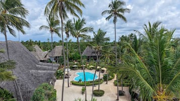 Un complexe hôtelier doté d’une piscine entourée de palmiers et de cabanes aux toits de chaume.