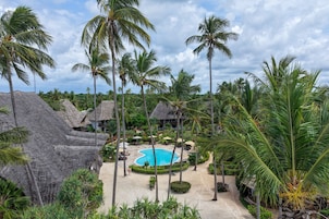 Un resort con piscina rodeada de palmeras y cabañas de techo de paja.