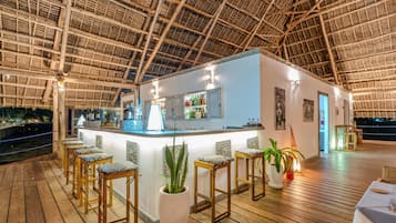 An outdoor bar area with a thatched roof, wooden stools, and a bar counter.