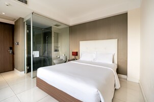 Habitación de hotel moderna con una cama grande, cabina de ducha de vidrio, inodoro y mesita de noche con lámpara.