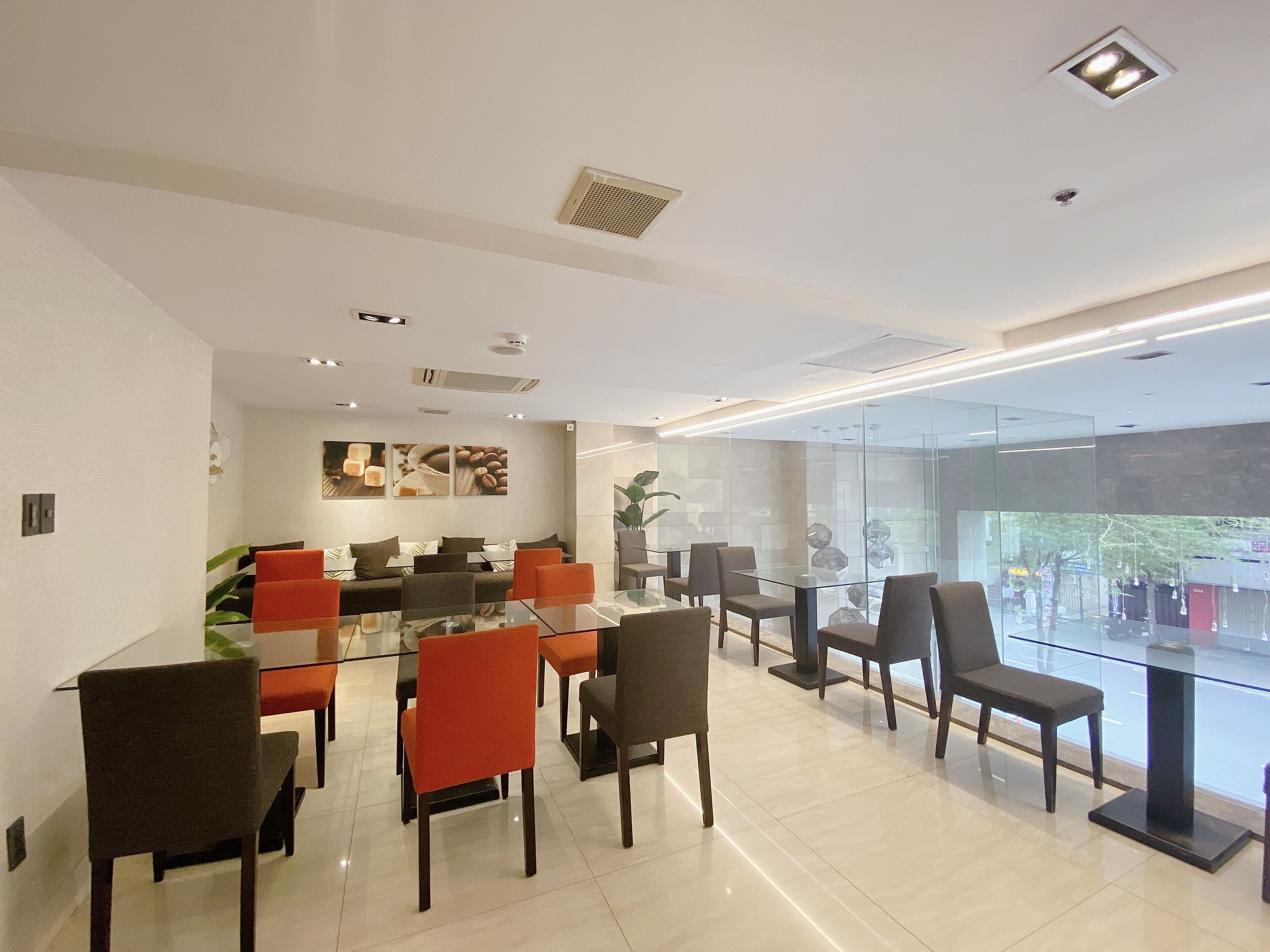 A modern dining area with glass tables and chairs, a sofa, and a coffee-themed wall art.