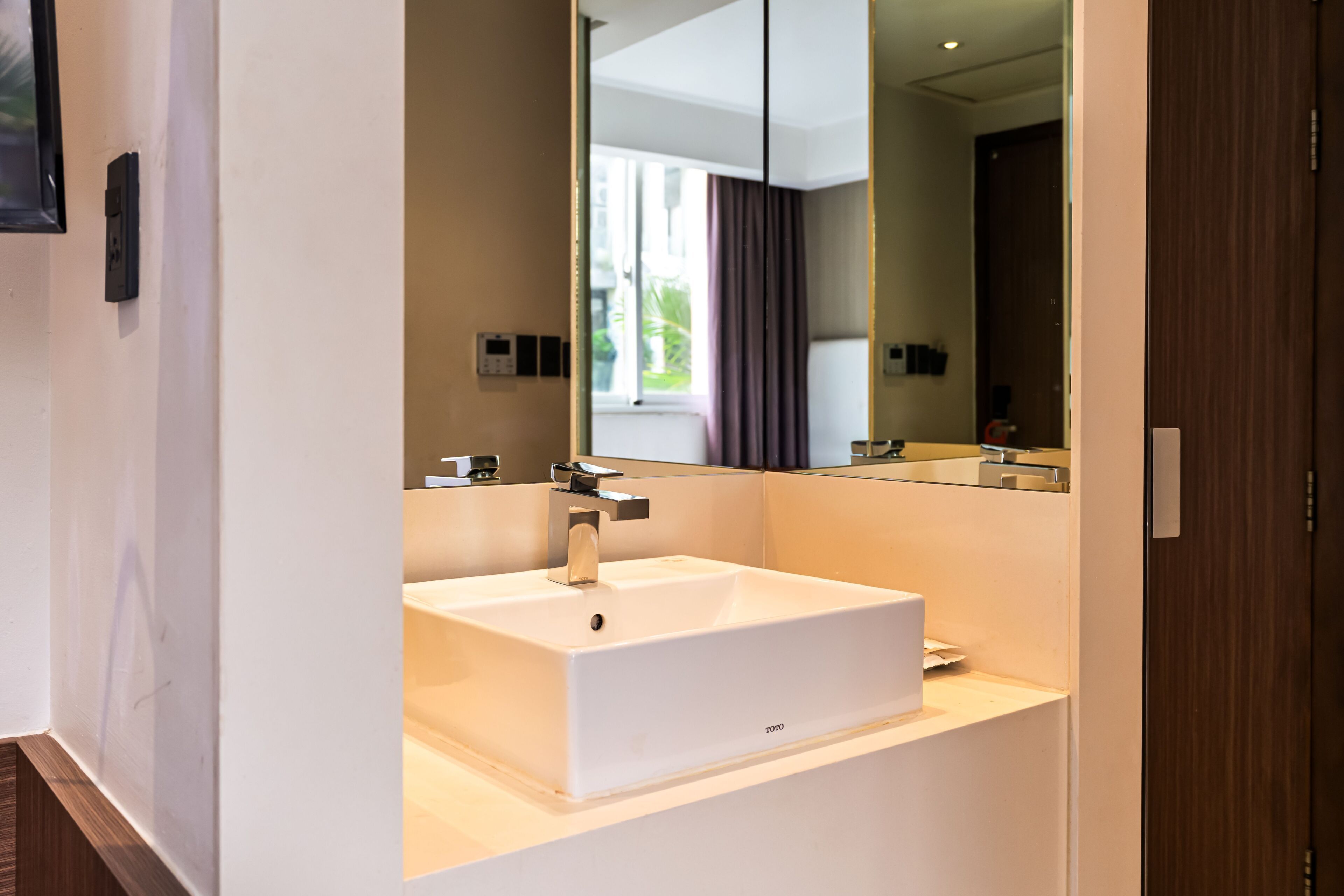 Un baño moderno con un lavamanos blanco, un espejo y una puerta.