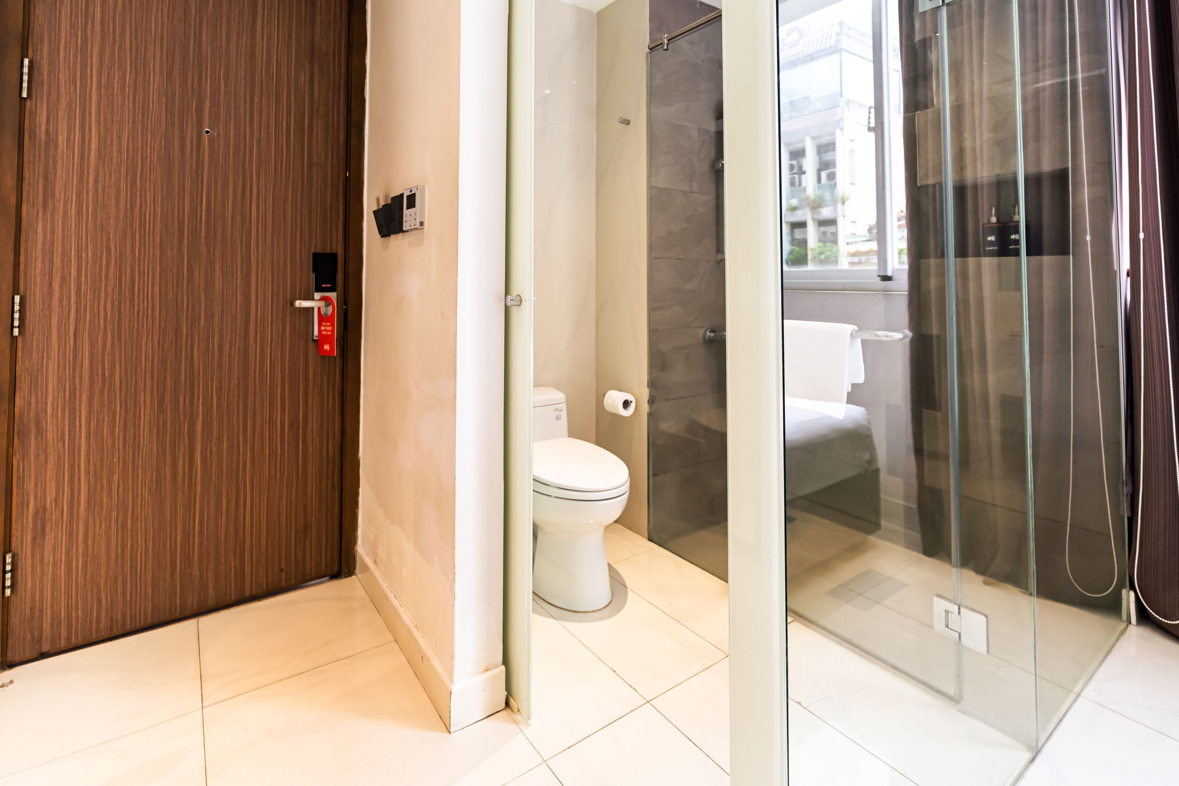 A modern bathroom with a wooden door, a toilet, a glass shower enclosure, and a visible window.
