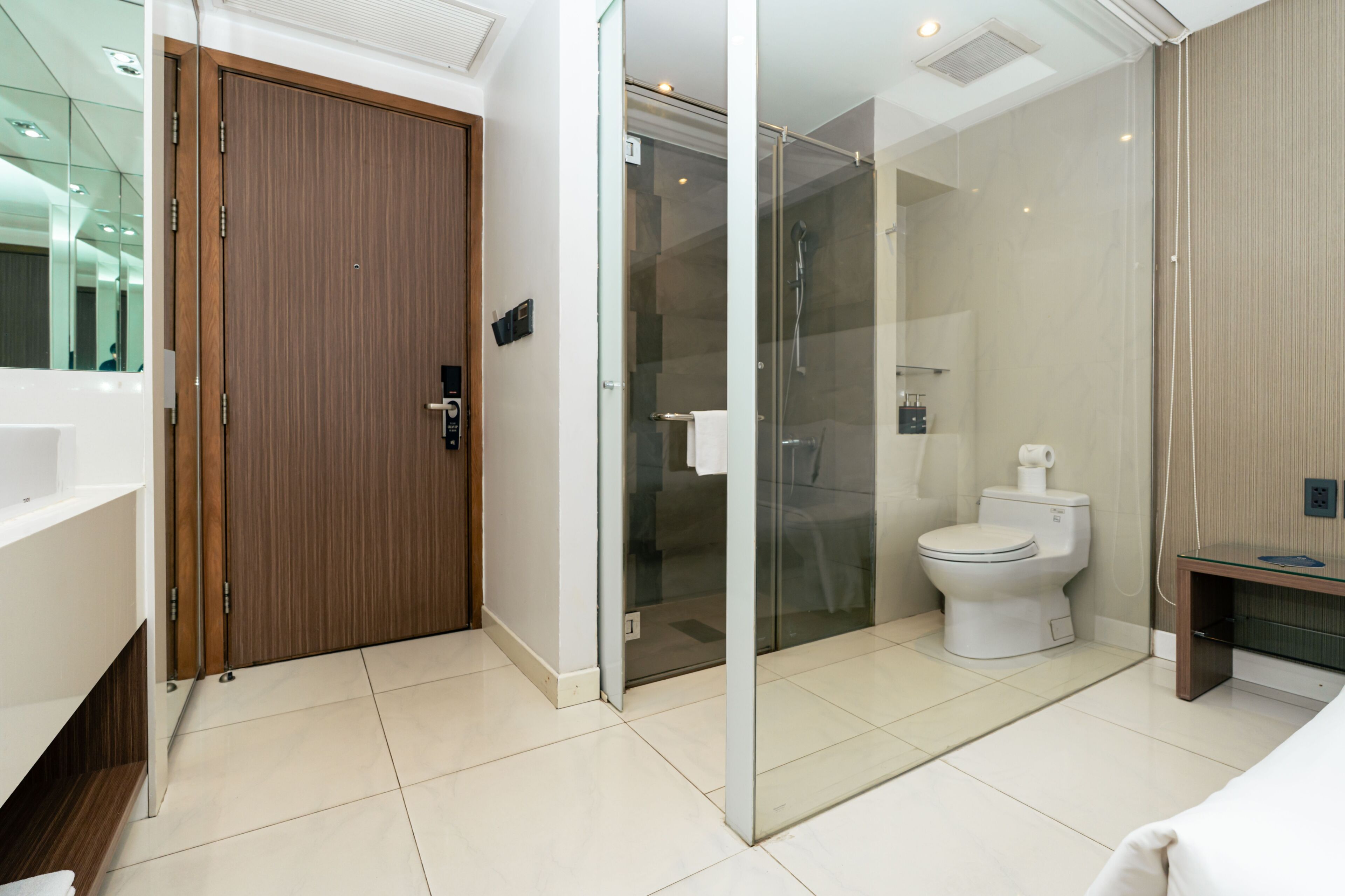 Een moderne badkamer met een houten deur, een douchecabine van glas, een wit toilet en een glazen wastafelmeubel.