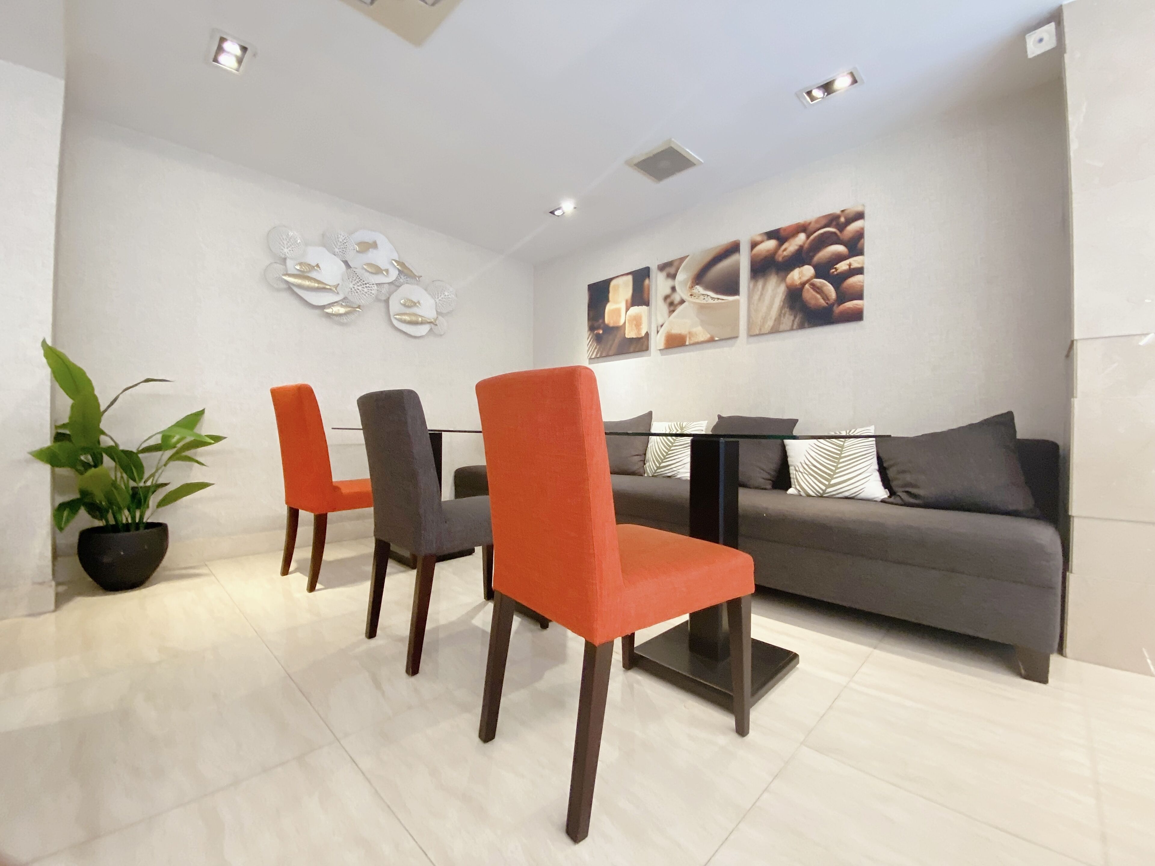 A modern living room with a grey sofa, orange chairs, a glass coffee table, and a potted plant.