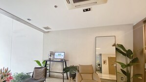 A modern living room with a glass coffee table, a beige armchair, a black desk with a laptop, and a large mirror. There are potted plants and a bookshelf with books. - Nicecy Ben Thanh Hotel (Ho Chi Minh City)