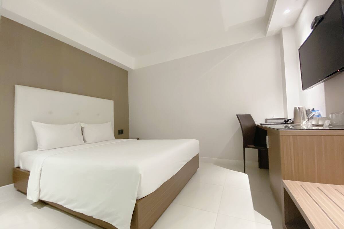 Une chambre d’hôtel moderne, dotée d’un grand lit, d’un bureau et d’un téléviseur à écran plat fixé au mur.