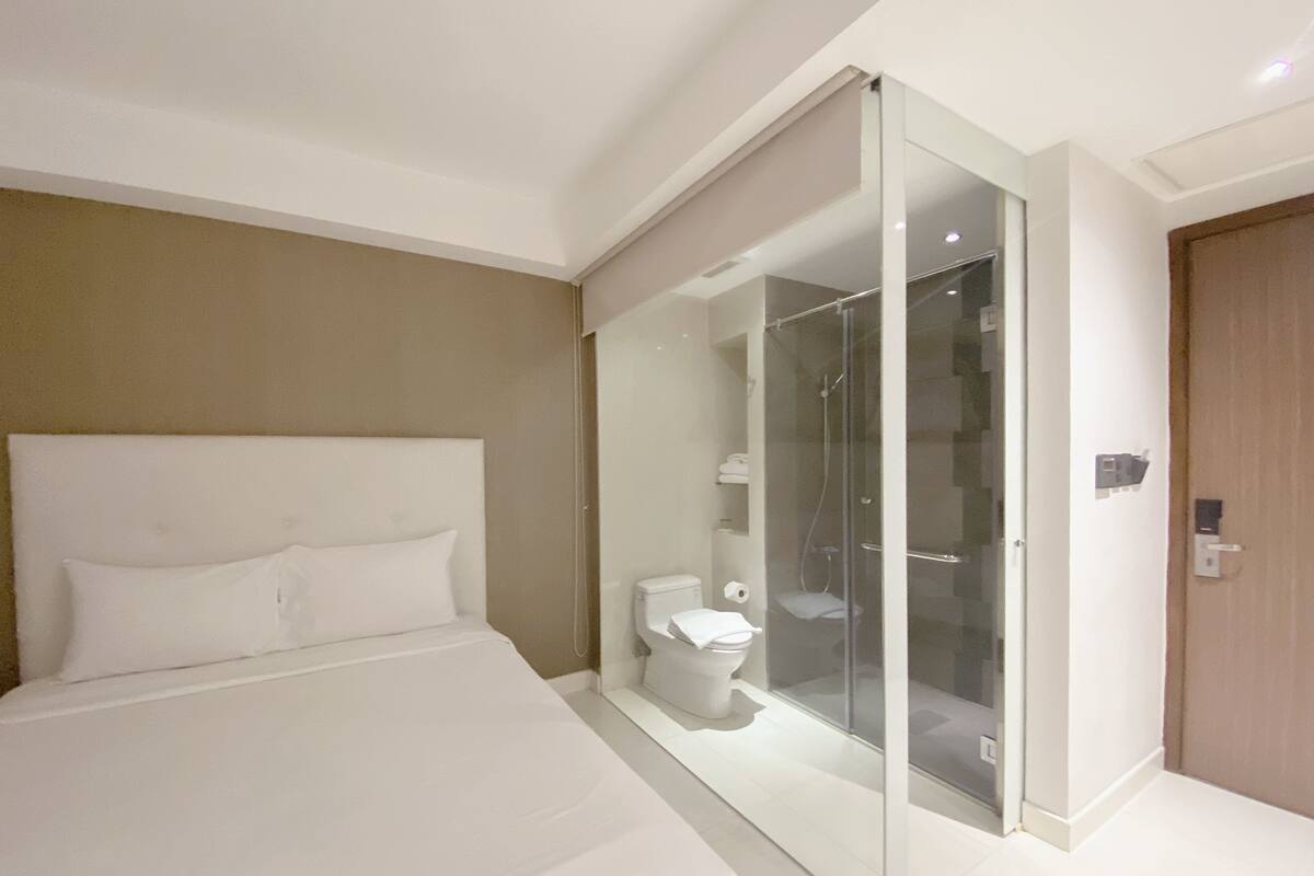 Une chambre d’hôtel moderne avec un grand lit, une douche en verre et une porte en bois.
