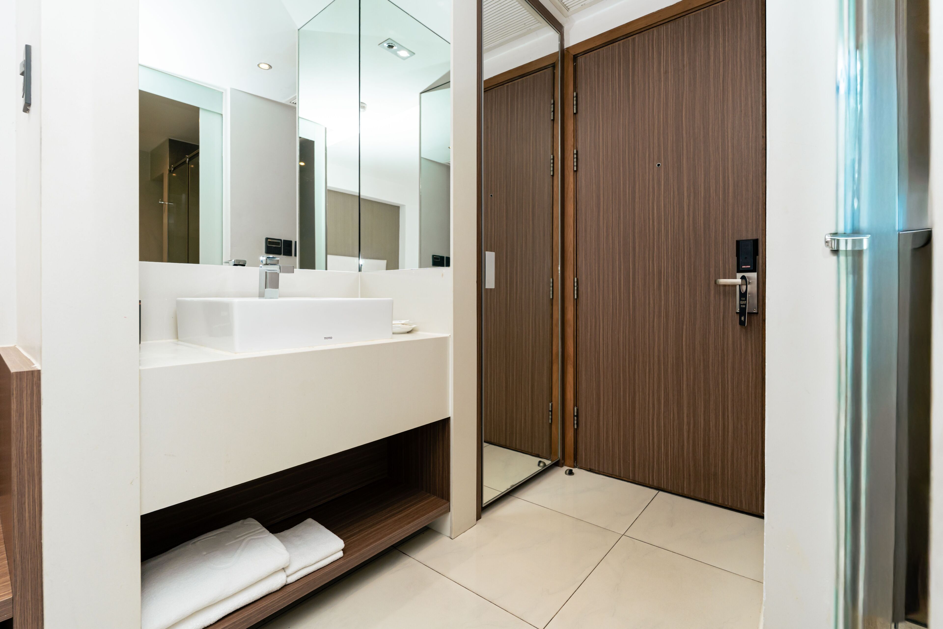 A modern bathroom with a white vanity, a mirror, and a wooden door.
