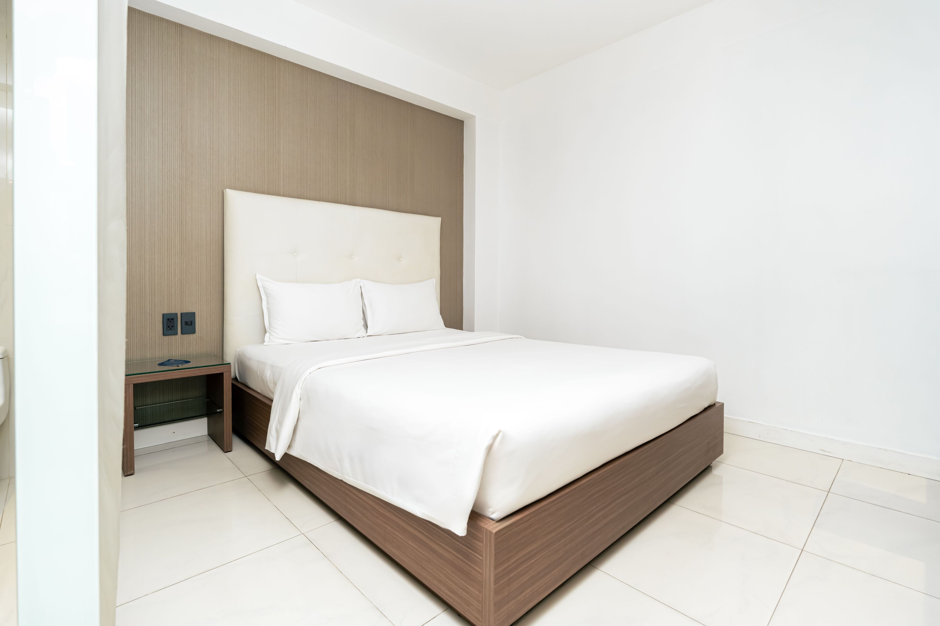 A modern bedroom with a large bed, a wooden headboard, a bedside table, and a nightstand.