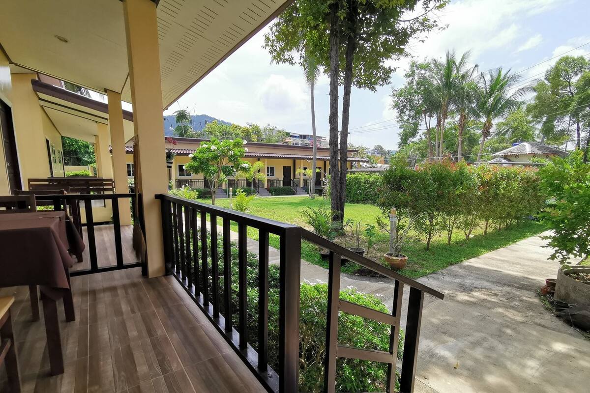 Un espacio al aire libre cubierto con suelo de madera, barandilla negra y vistas a un área residencial con casas y vegetación.