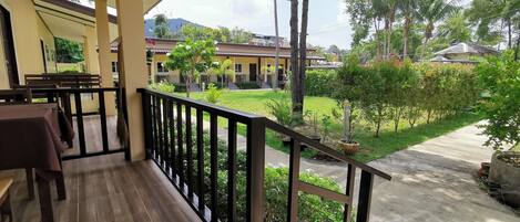 A covered outdoor area with wooden flooring, a black railing, and a view of a residential area with houses and greenery.