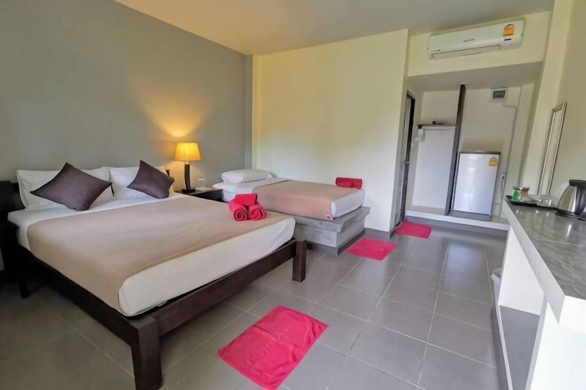 Habitación de hotel con cama, mesita de noche, escritorio, refrigerador y baño visible a través de una puerta abierta.