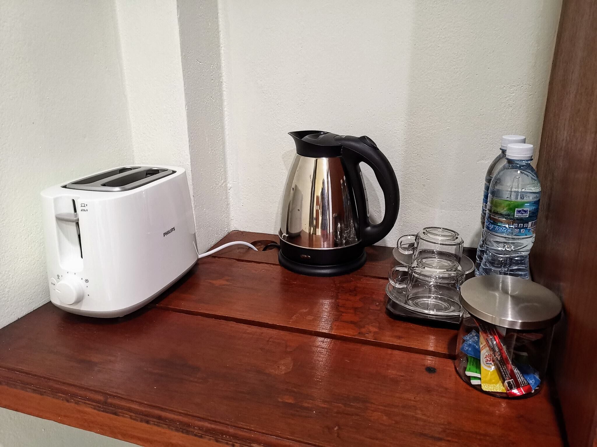 A small kitchenette with a white Philips toaster, a black electric kettle, a water bottle, and a glass jar with snacks.