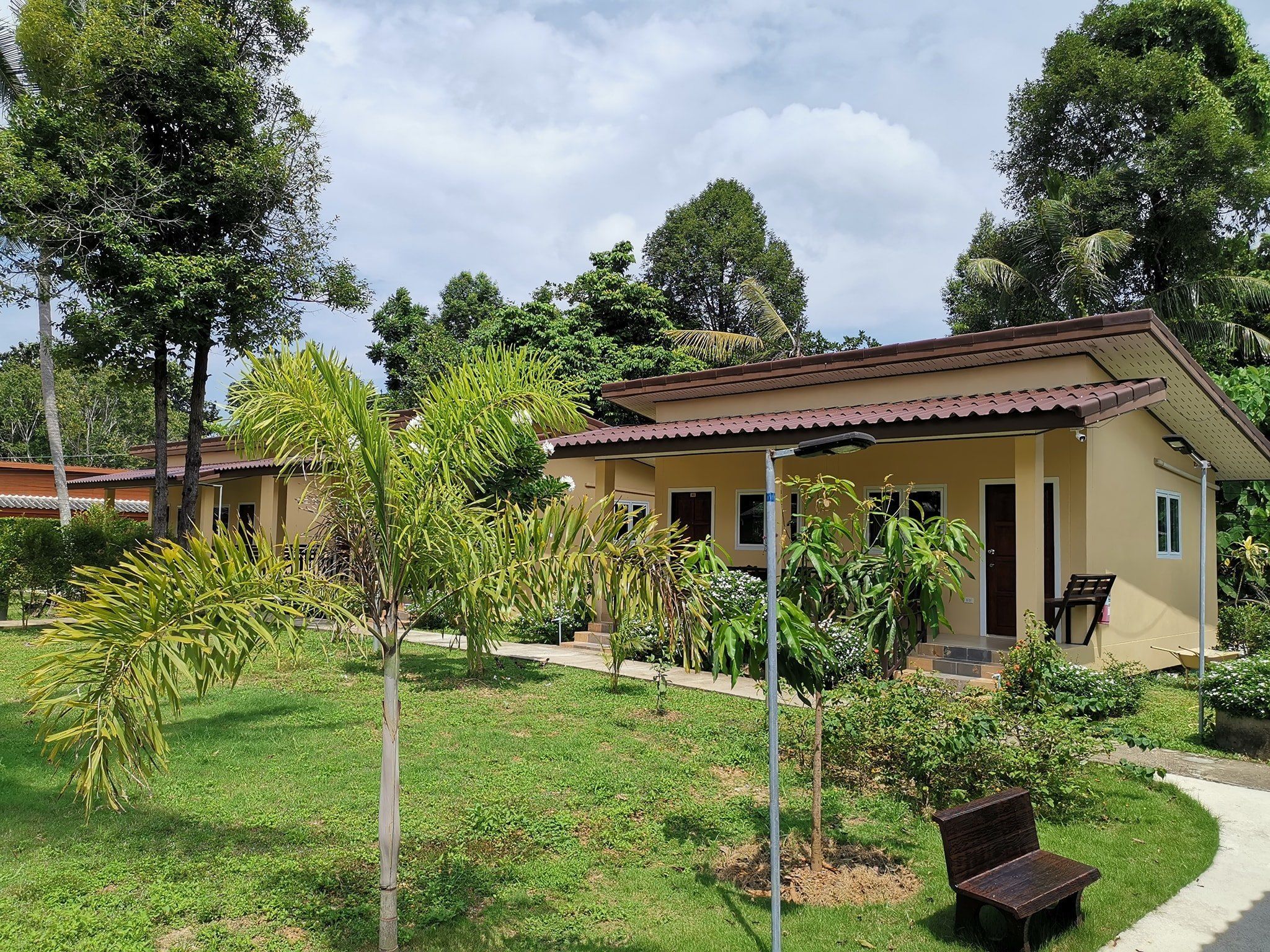 A single-story building with a tiled roof, surrounded by a well-maintained garden with various plants and a bench.
