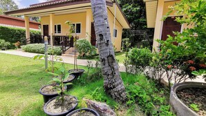 A yellow building with a covered patio area, potted plants, and a well-maintained lawn. - Ser-En-Dip-I-Ty (Ko Lanta)