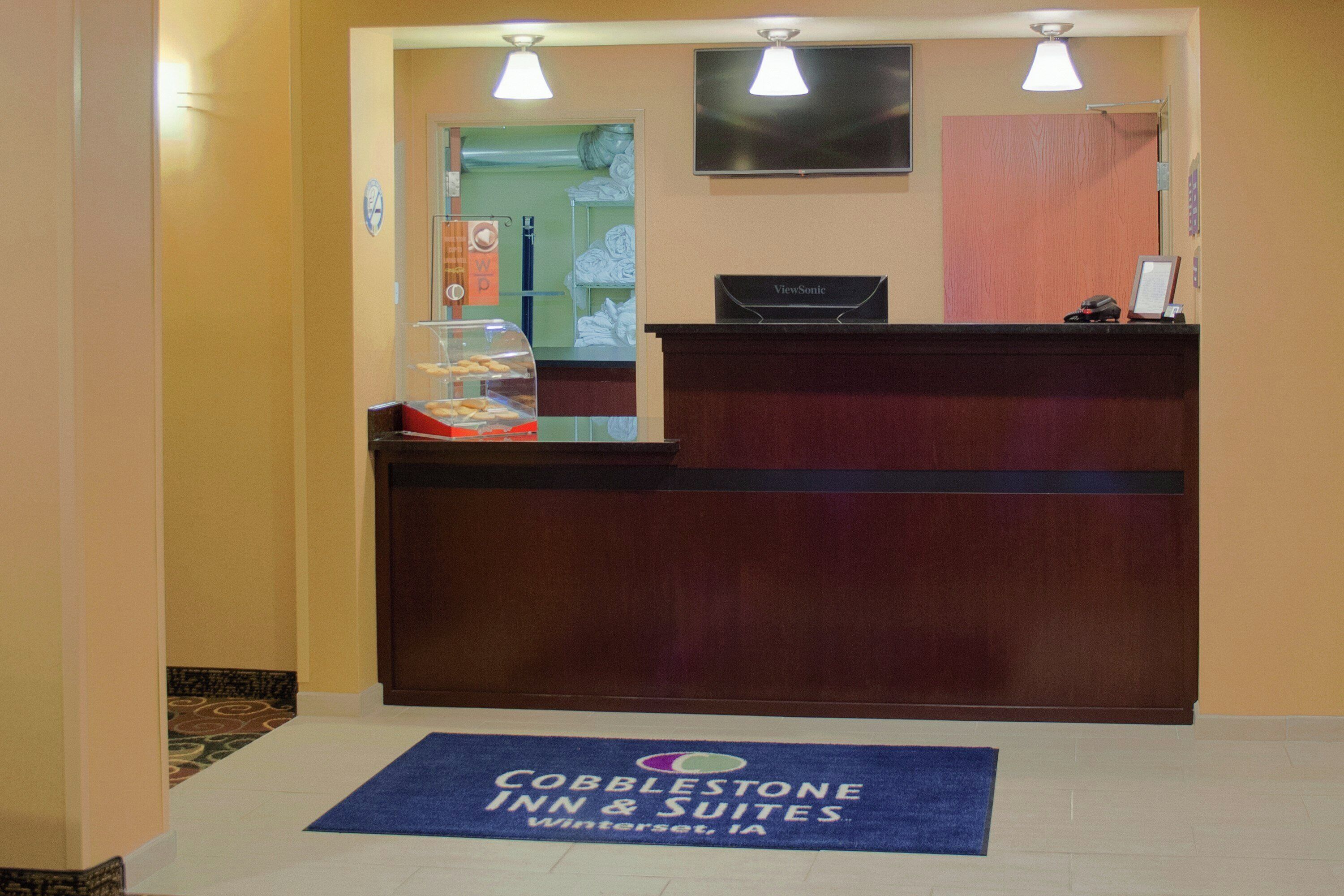 A reception desk with a sign for Cobblestone Inn & Suites, a glass display case with items, and a blue mat on the floor.